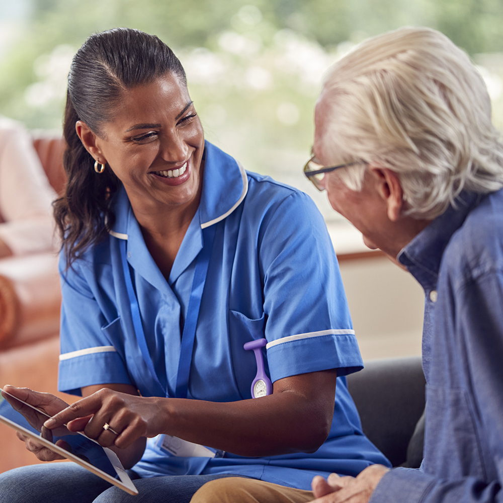 A nurse in a blue uniform showing information on a tablet to an elderly man.